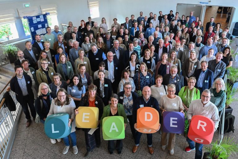 Teilnehmende der Landgespräche mit bunten LEADER-Würfeln Gruppenfoto mit Teilnehmern, die "LEADER" in bunten Buchstaben halten.