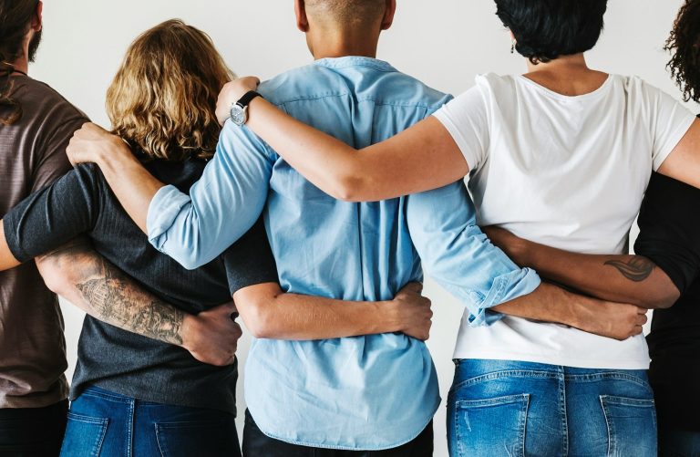 Gruppe von vier Personen im Halbprofil, Arme umeinander gelegt, von hinten gesehen